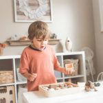 Child Learning - boy in orange crew neck t-shirt standing in front of white wooden table with cupcakes