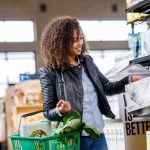 Grocery Shopping - A woman carrying a grocery basket of vegetables picks up a Boxed Water box