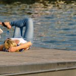 Leisure Time - woman in white tank top and gray pants lying on brown wooden dock during daytime