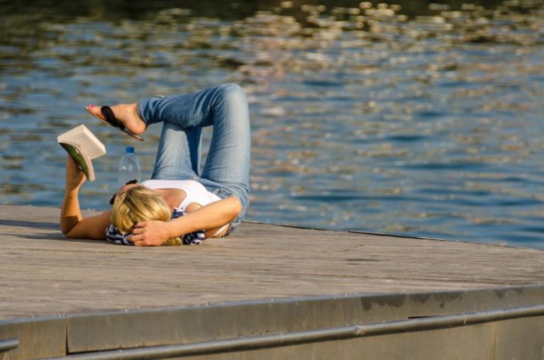 Leisure Time - woman in white tank top and gray pants lying on brown wooden dock during daytime
