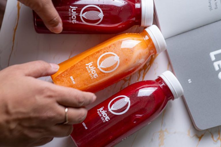 Healthy Smoothies - a person holding a bottle of orange juice next to a laptop