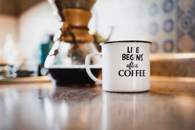 Morning Coffee - white and black life begins after coffee printed enamel cup beside 1/4 black liquid-filled glass flask on brown wooden panel